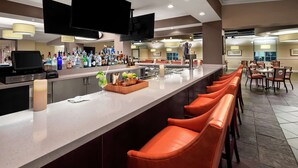 Un espace bar doté d’un long comptoir, de nombreuses bouteilles d’alcool, d’un téléviseur et de tabourets de bar orange.