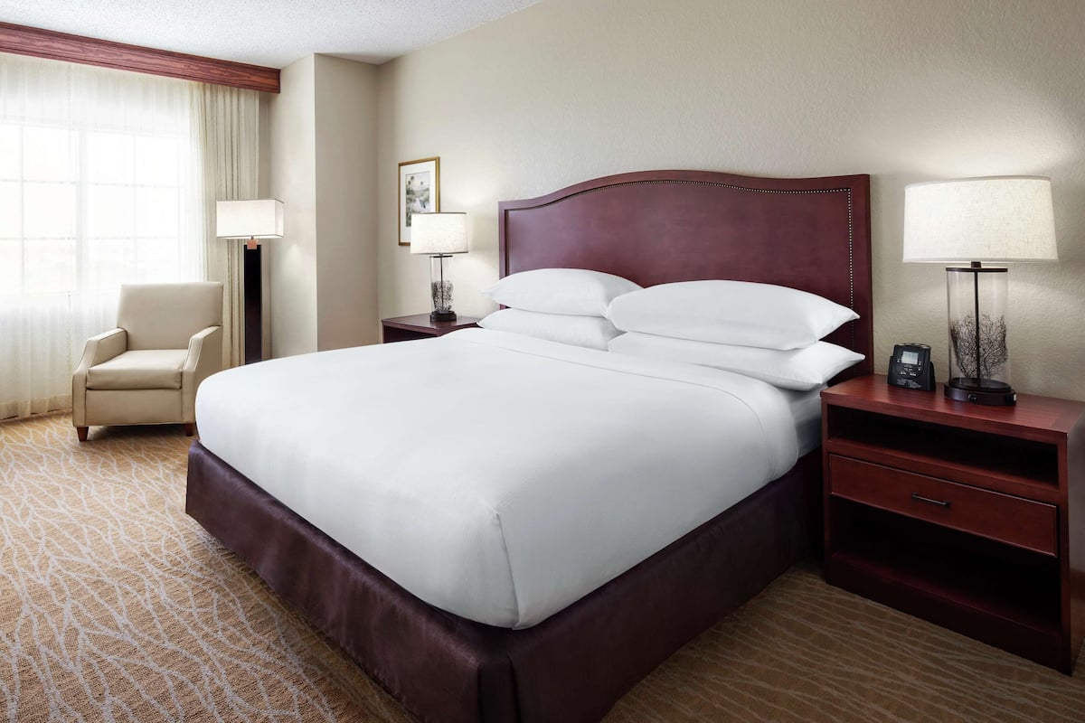Une chambre d’hôtel avec un grand lit, un bureau avec une chaise, une table de chevet avec une lampe et une fenêtre avec des rideaux.
