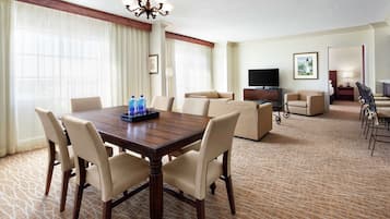 Habitación de hotel con zona de comedor, sofá, televisión y piso alfombrado.