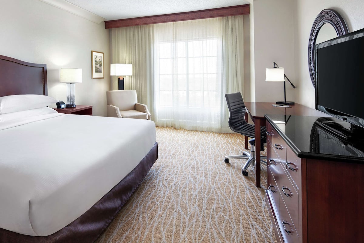 Une chambre d’hôtel avec un grand lit, un bureau avec une chaise, une télévision et une fenêtre avec des rideaux.