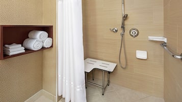 A bathroom with a shower, a towel rack with towels, a small table, and a toilet.