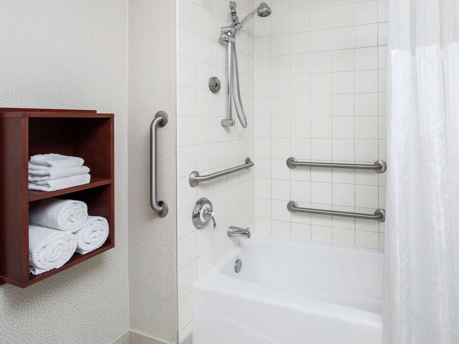 A bathroom with a white bathtub, a shower with a handheld showerhead, and a towel rack with folded towels.