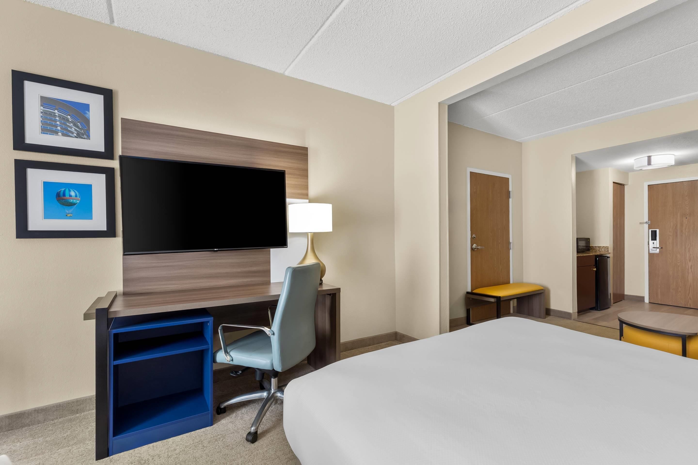 Een hotelkamer met een bed, een bureau met stoel, een televisie en een kleine kitchenette.