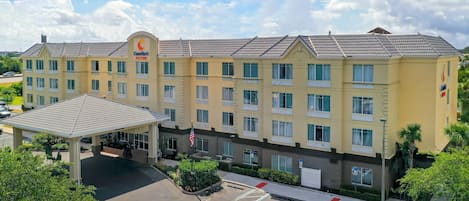 Un hotel de varios pisos con entrada cubierta, estacionamiento y espacios reservados para personas con discapacidad, e izamiento de la bandera estadounidense.