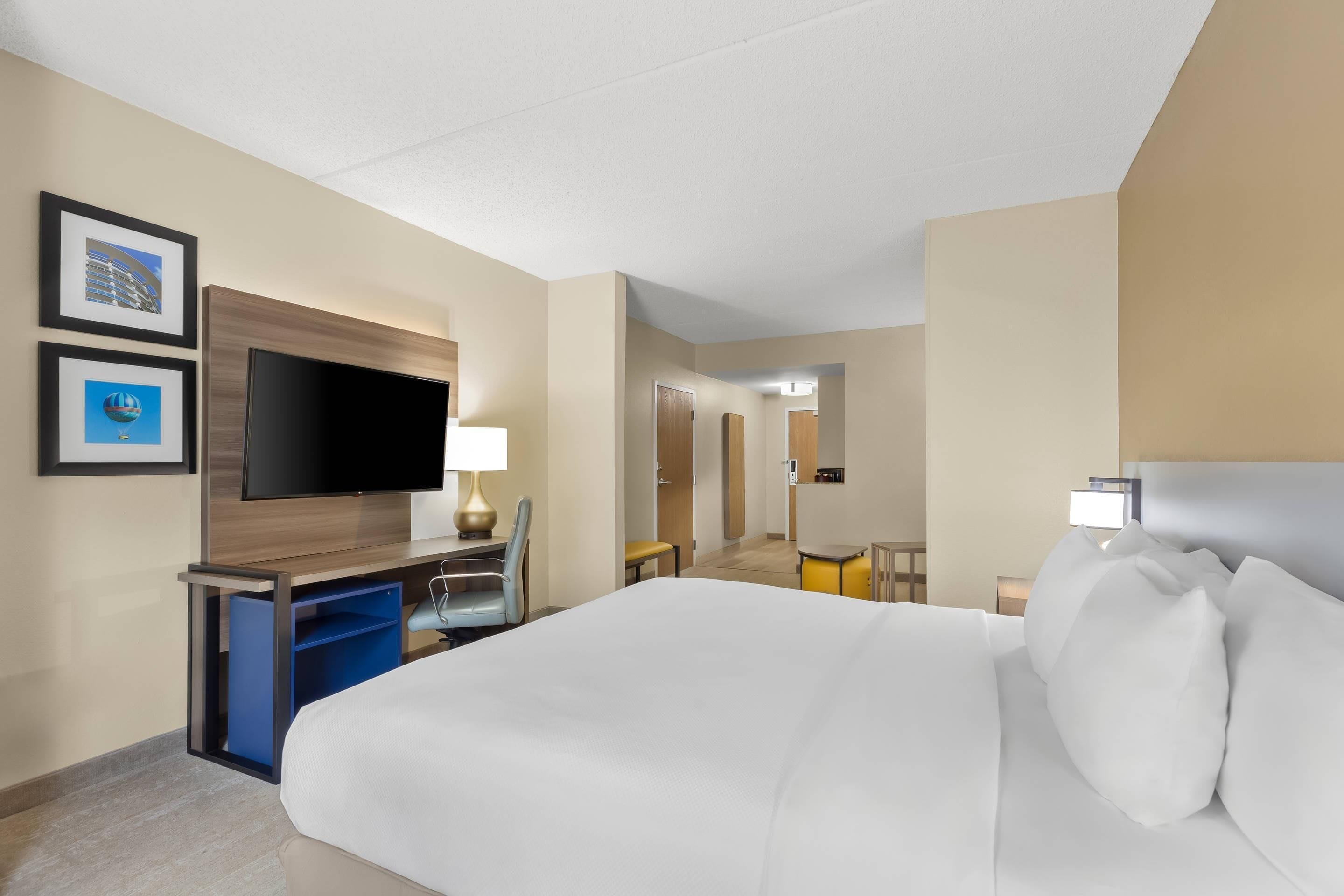 Ein Hotelzimmer mit einem Bett, einem Schreibtisch, einem Flachbildfernseher, einem Sessel und einem kleinen Tisch.