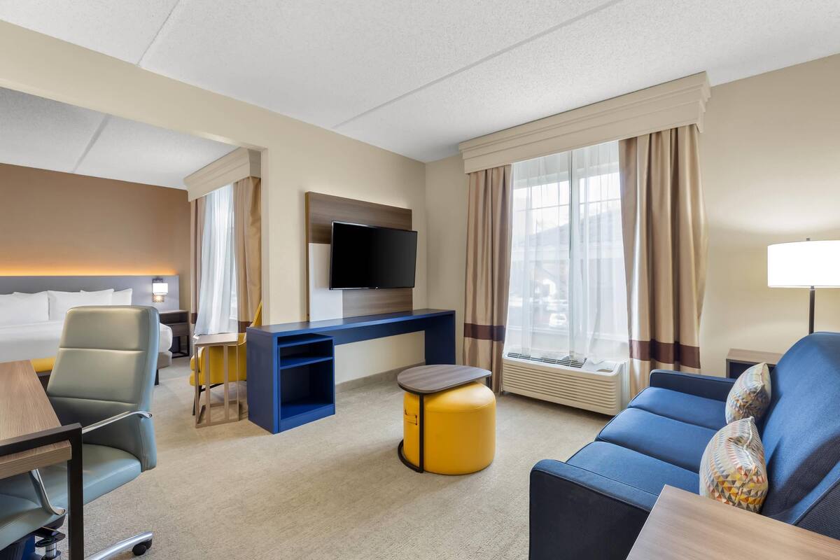 Une chambre d’hôtel avec un lit, un bureau, une télévision, un canapé et une fenêtre avec des rideaux.