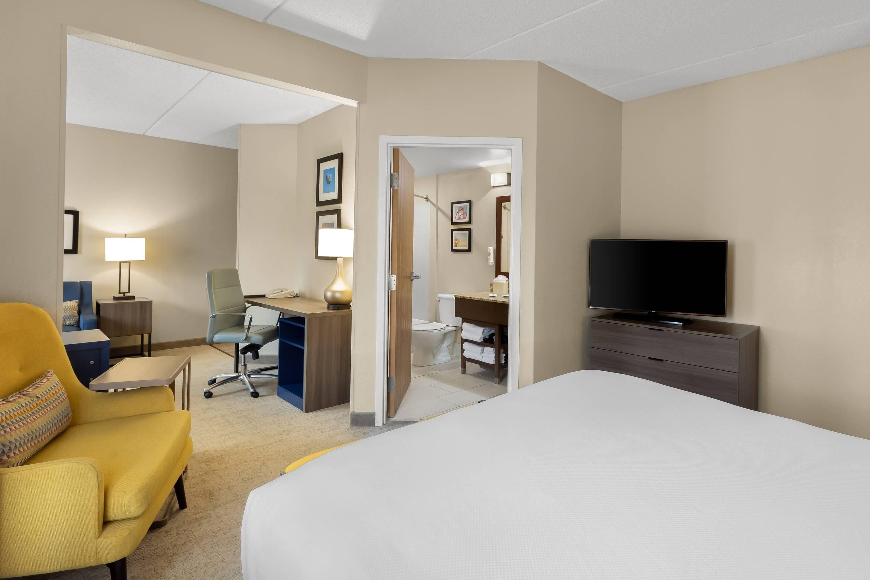 Une chambre d’hôtel avec un lit, un bureau, une chaise, une télévision et une salle de bain visible à travers une porte ouverte.