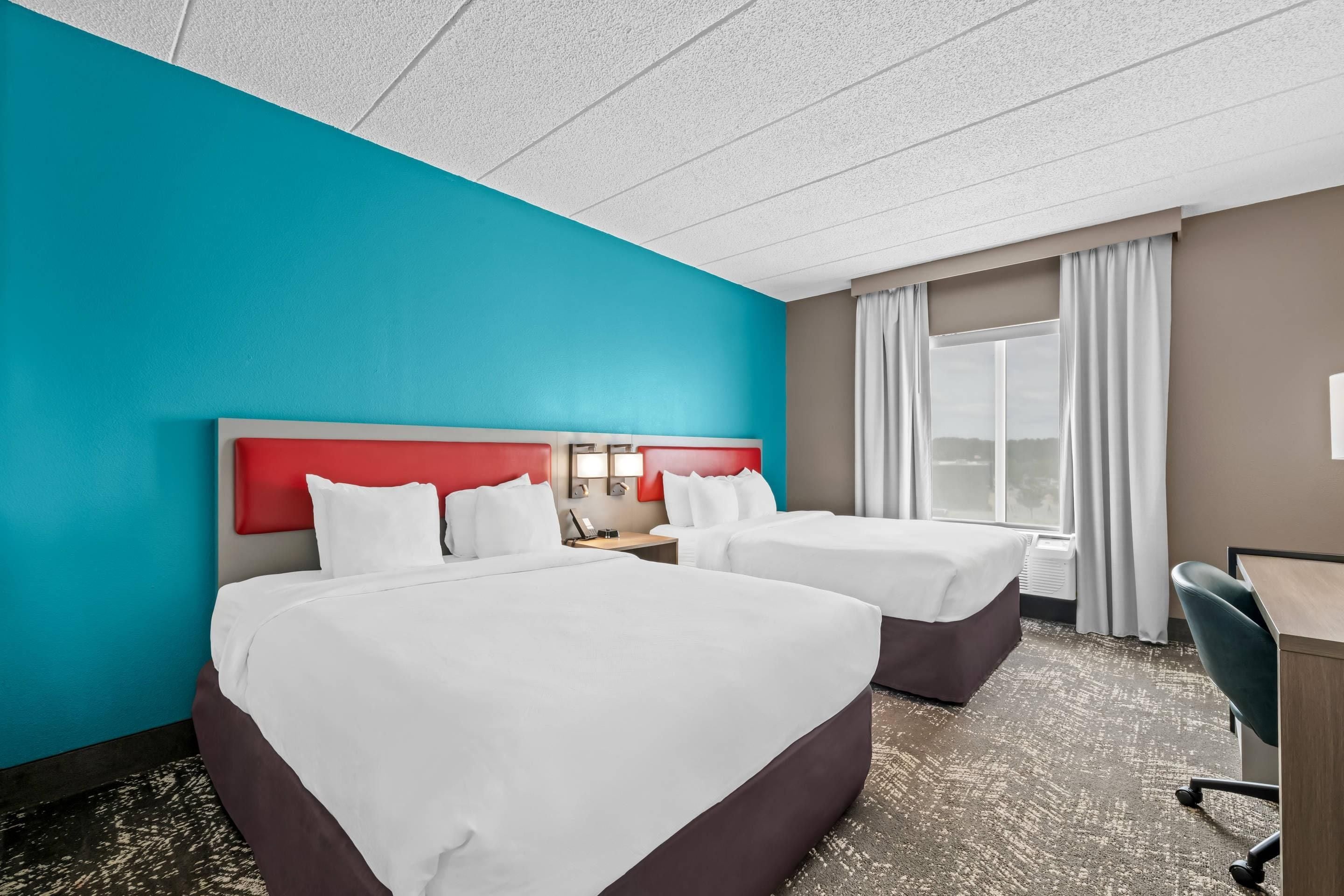 A hotel room with two beds, a desk, and a window with curtains.