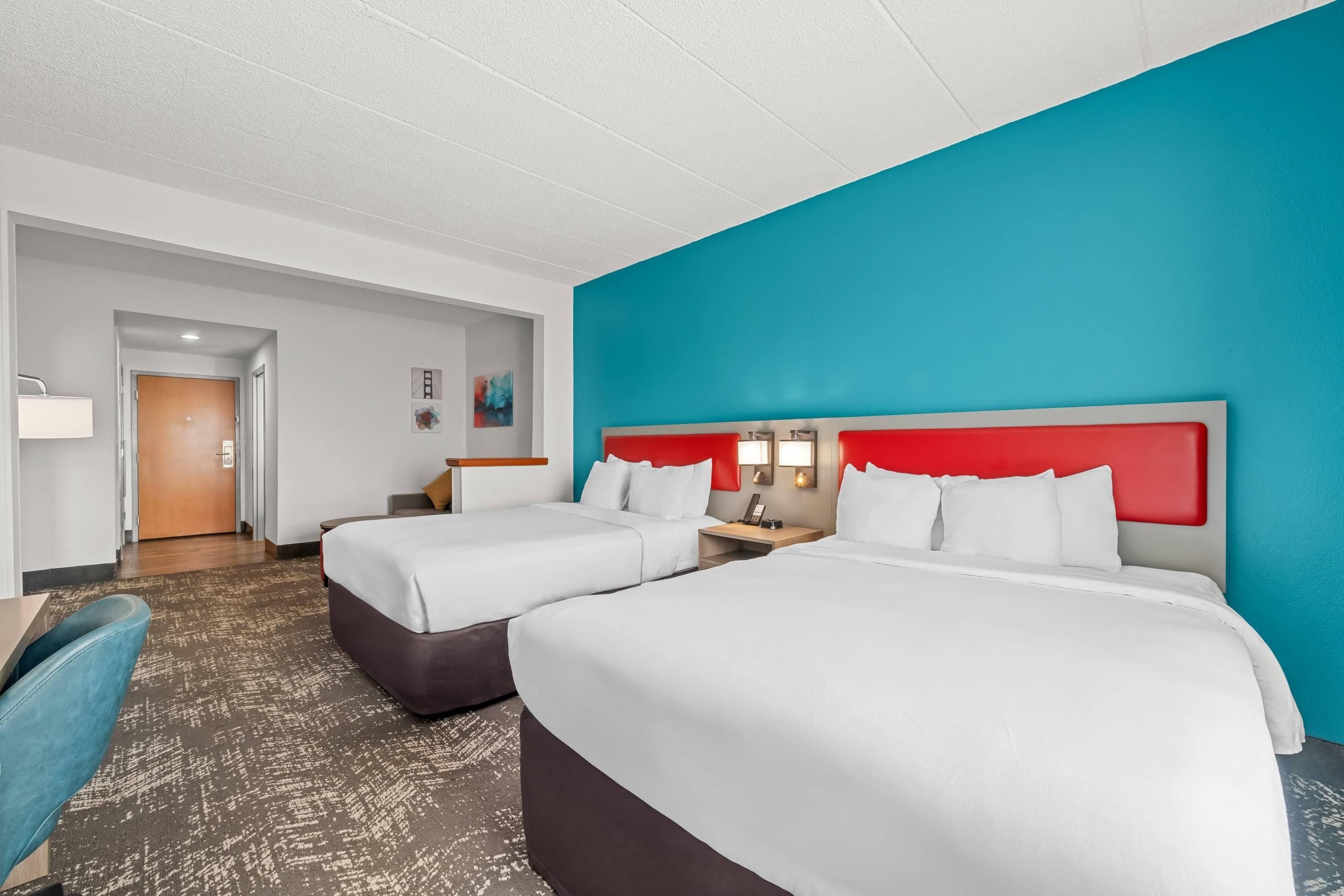Una camera d'albergo con due letti, una scrivania, una sedia e un bagno.