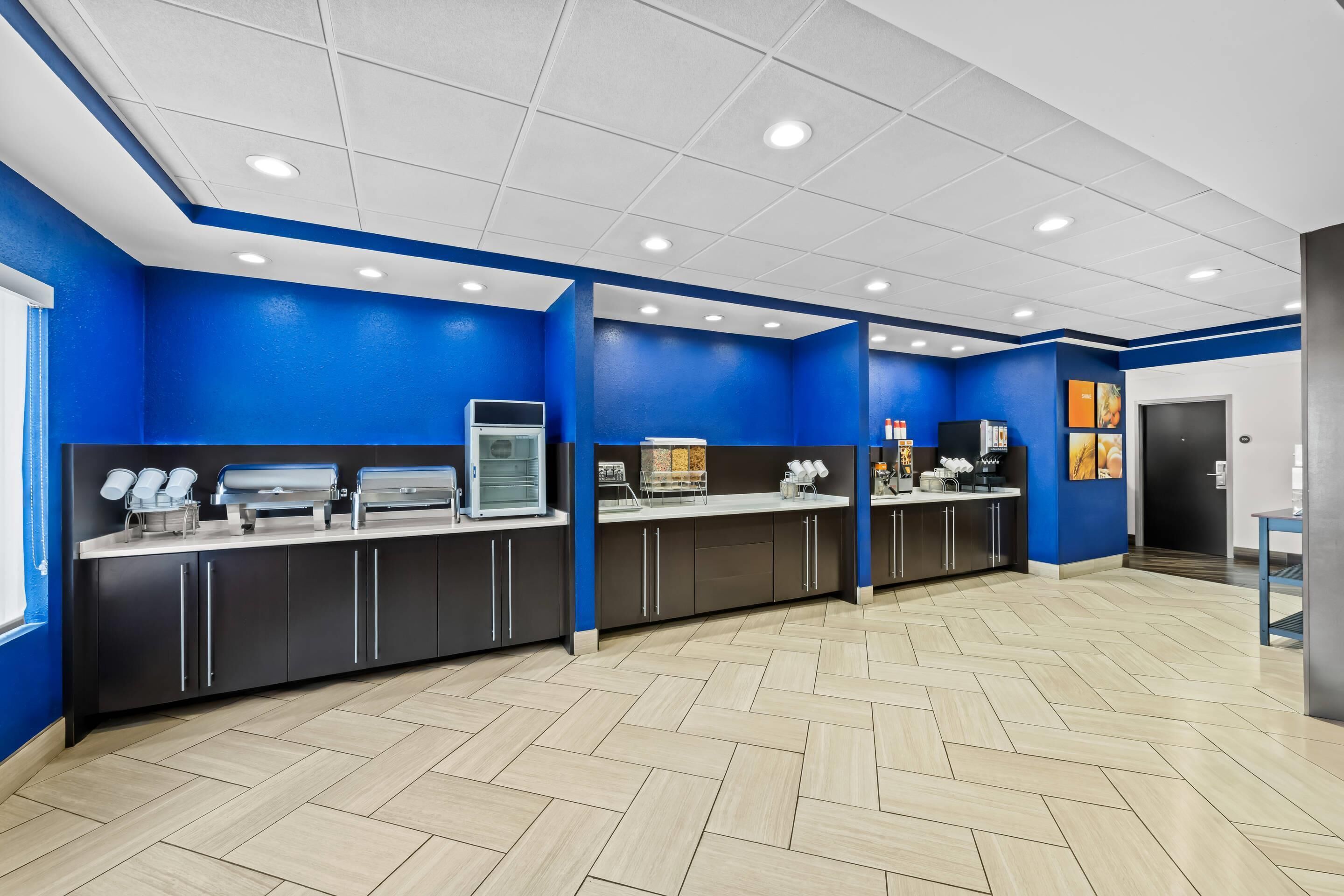 A modern kitchen area with blue walls, stainless steel appliances, and a herringbone floor pattern.