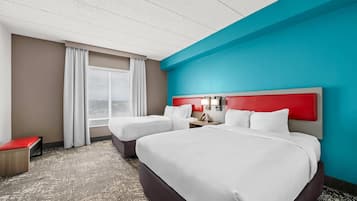 Habitación de hotel con dos camas, un banco rojo, una ventana con cortinas y vistas al exterior.