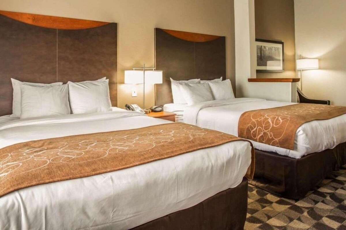 A hotel room with two beds, a nightstand with a phone, a lamp, and a painting on the wall.