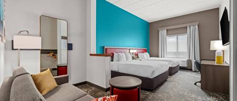 A hotel room with a large bed, a sofa, a small table, a mirror, and a television.