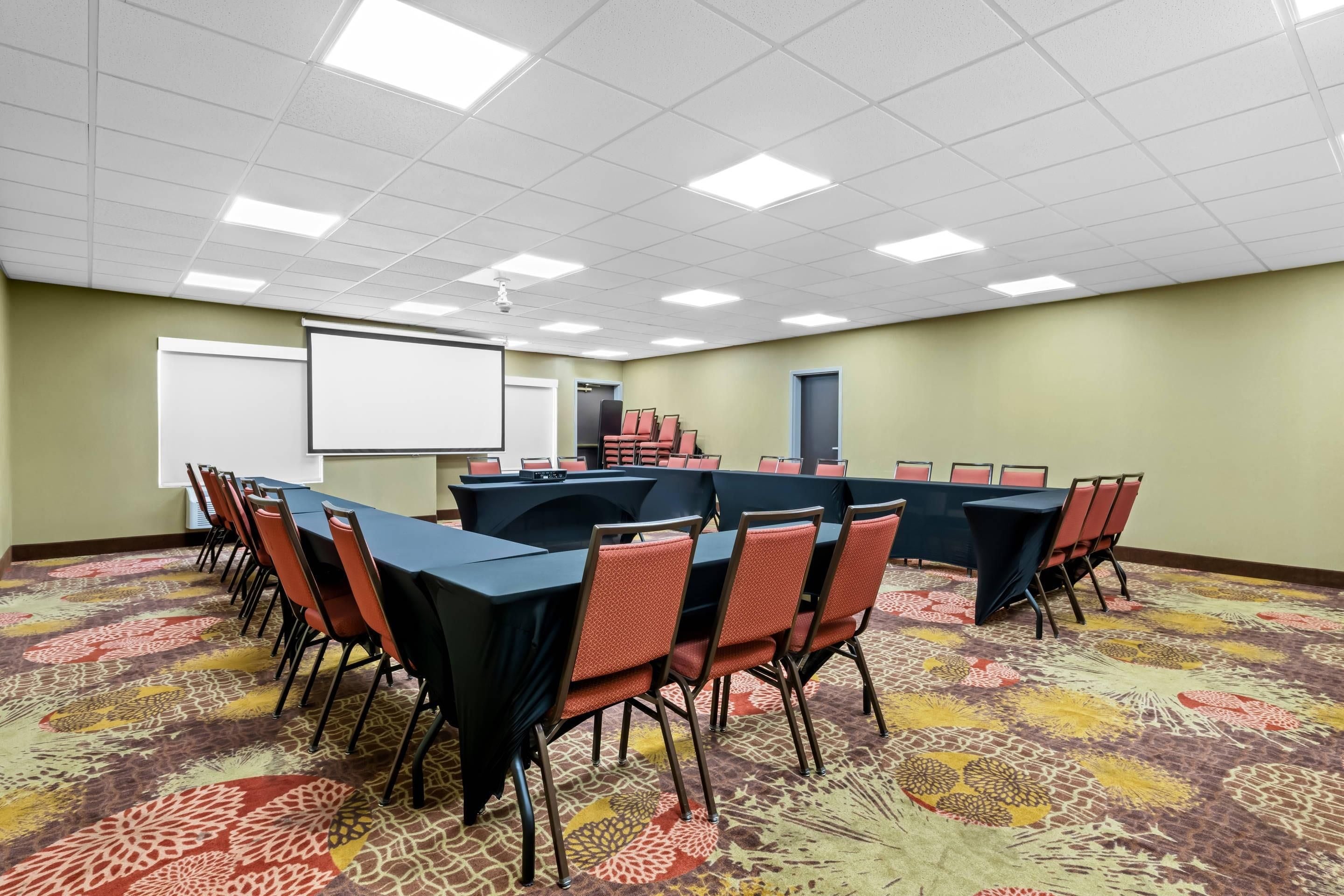A conference room with a large table, chairs, a projector screen, and a carpeted floor.