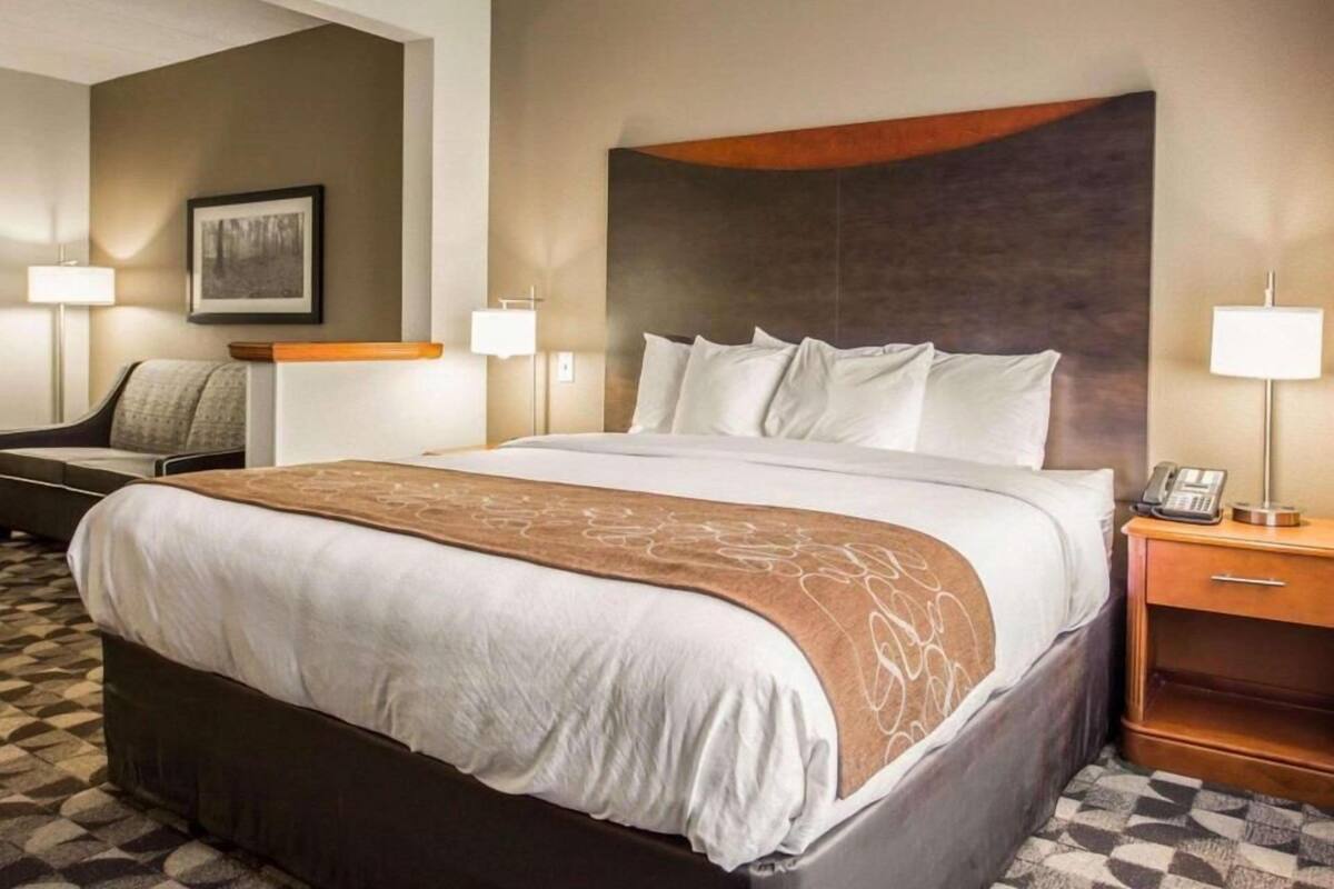 A hotel room with a large bed, a desk, a chair, and a lamp.