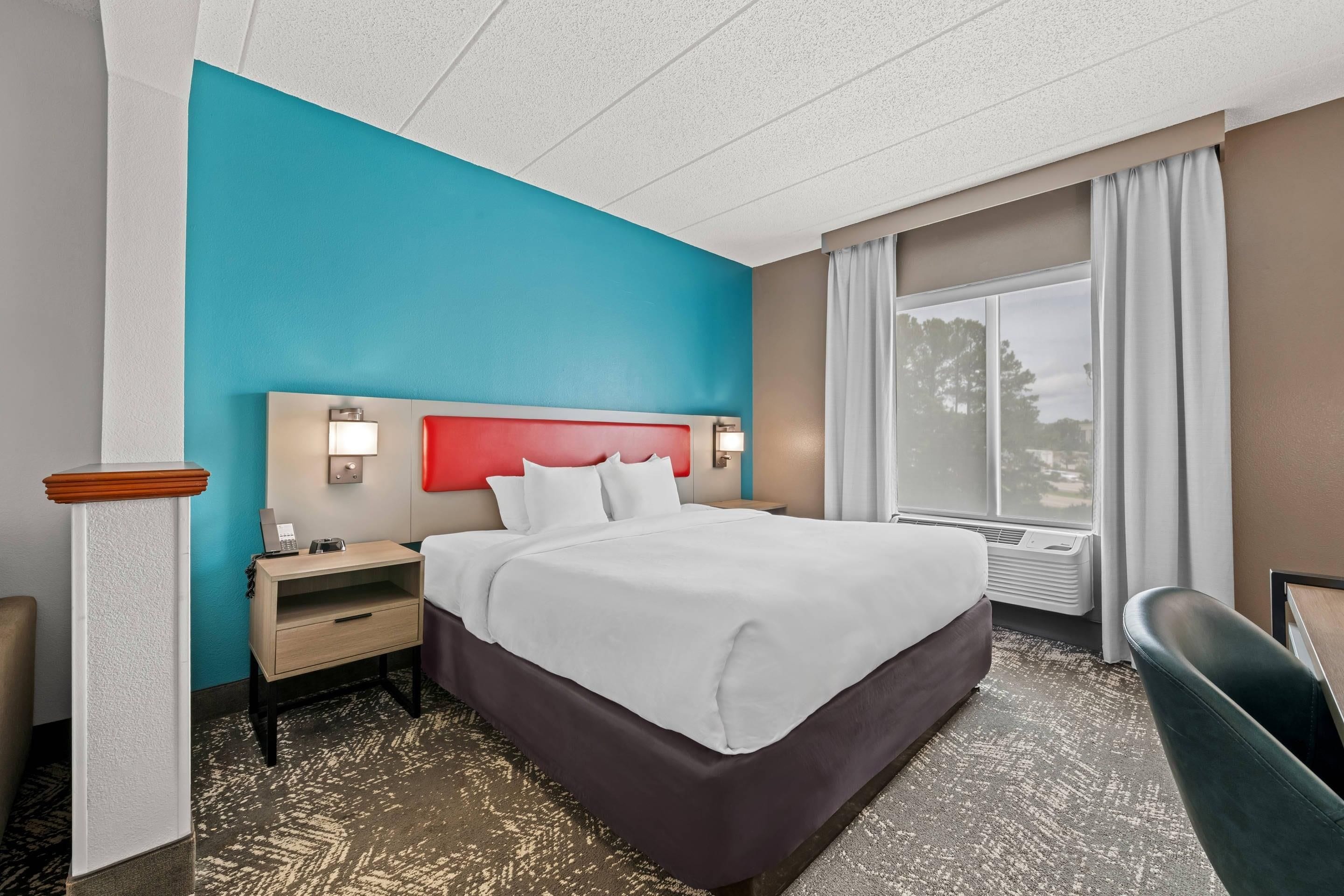 A hotel room with a bed, bedside tables, a desk, a chair, and a window with curtains.
