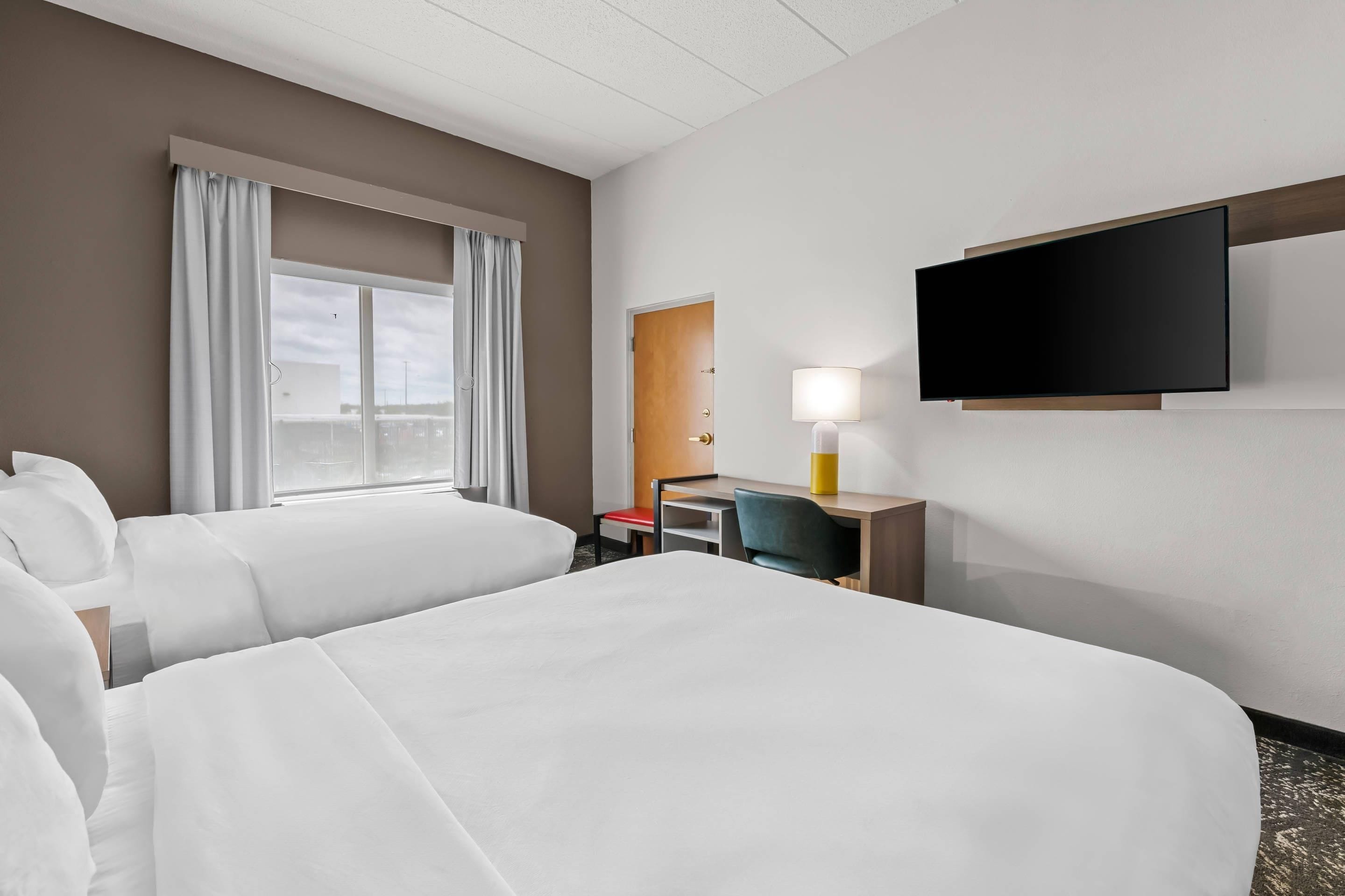 A hotel room with two beds, a desk, a chair, a TV, and a window with curtains.