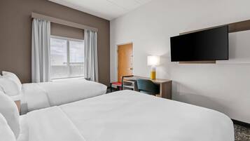A hotel room with two beds, a desk, a chair, a TV, and a window with curtains.