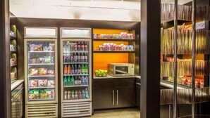 A compact kitchenette with two refrigerators stocked with beverages and snacks, a microwave, and shelves with packaged goods. - Comfort Suites Columbia at Harbison (Columbia)