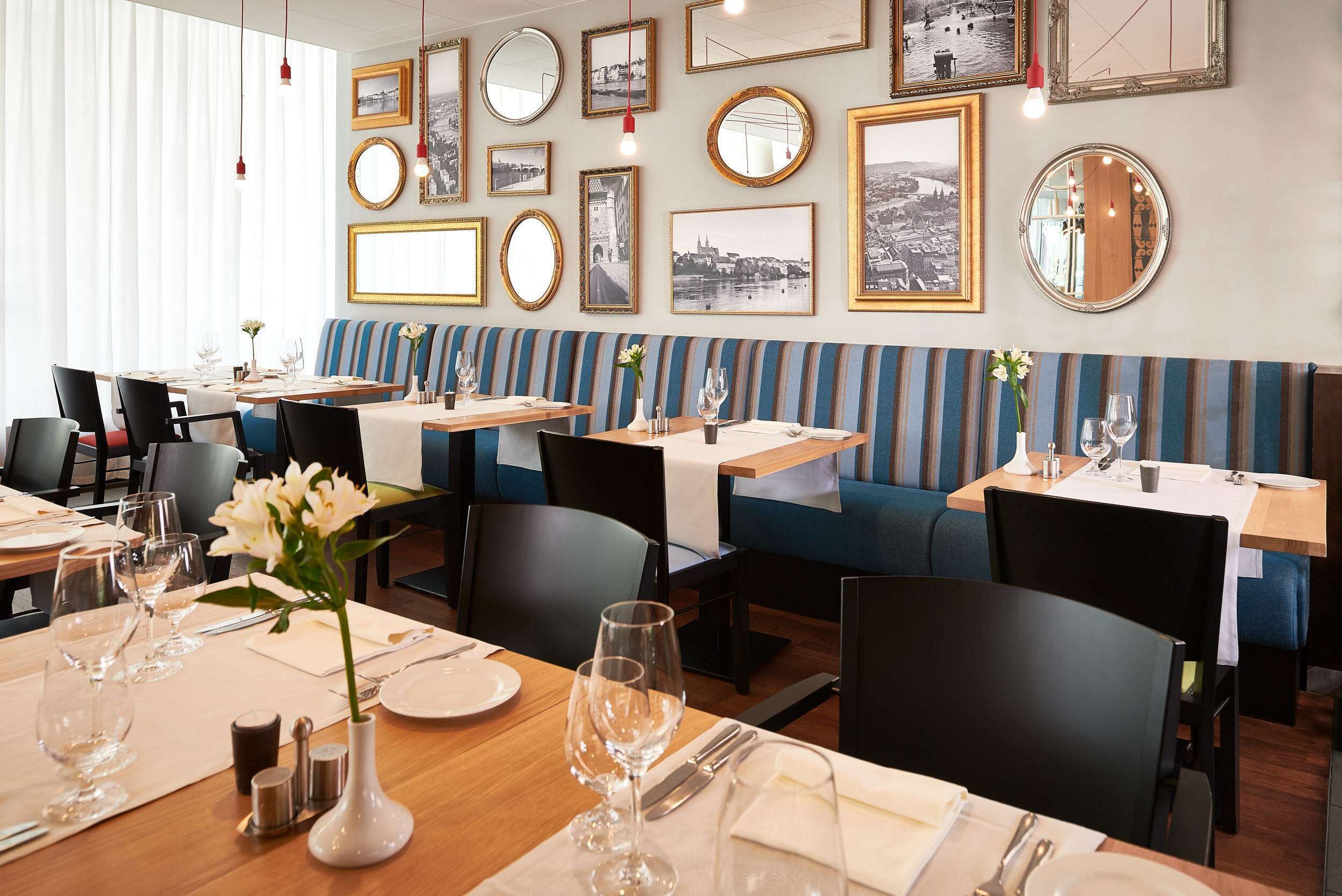 Un restaurante con varias mesas, cada una con copas de vino, platos y cubiertos. Hay bancos acolchados a rayas azul y blanco a lo largo de la pared.