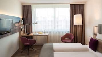 A hotel room with a bed, a desk with a chair, a TV, and a window with curtains.
