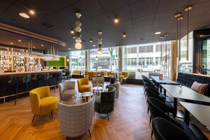 A modern bar area with a variety of seating options, including bar stools and cushioned chairs, and a large window providing a view of the street. - Essential by Dorint Basel City  (Basel)