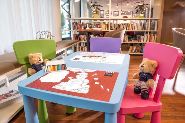 A children's table with a Kinder-Mond coloring book, two teddy bears, and a bookshelf in the background.