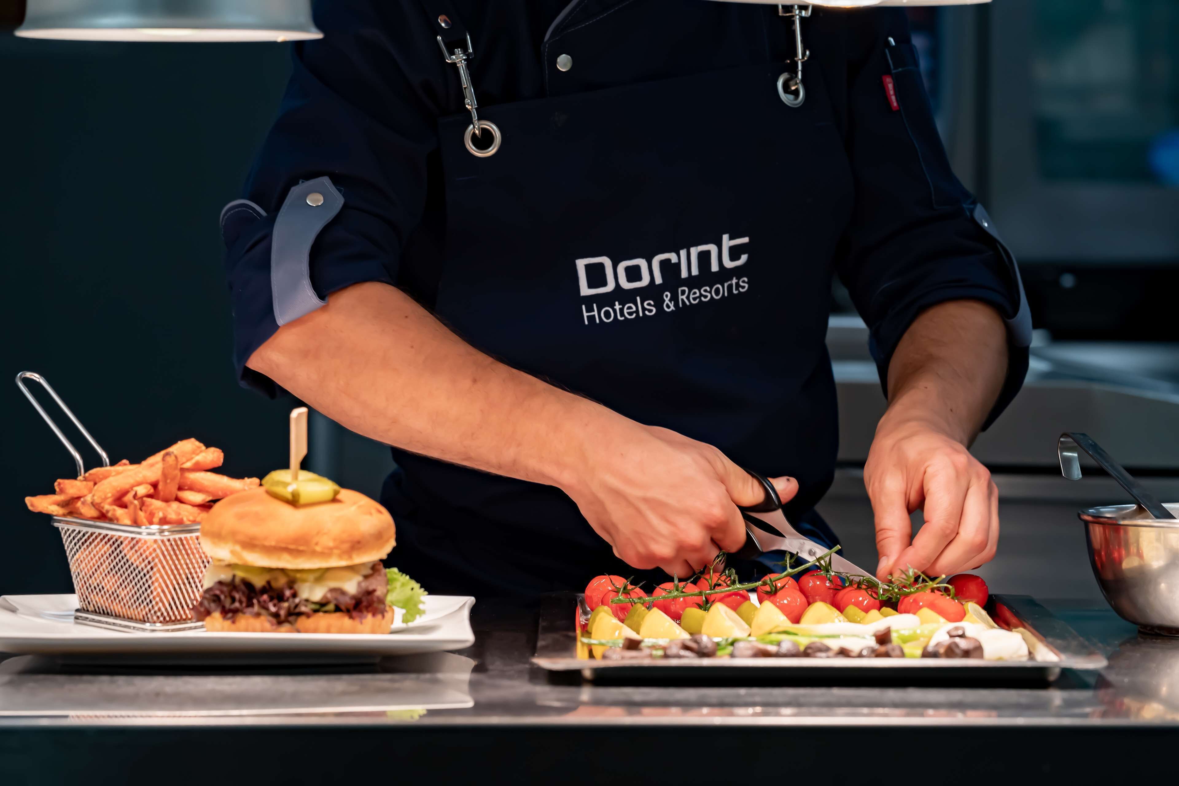 A person in a dark apron with "Dorint Hotels & Resorts" text, preparing food on a counter.