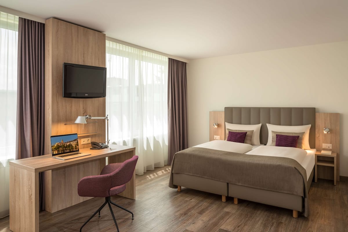 A hotel room with a bed, desk, chair, TV, and curtains.