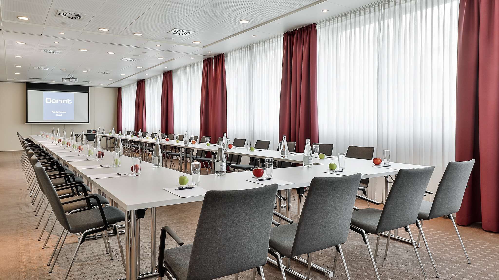 A conference room with long tables, grey chairs, and a projector screen displaying "Dorint."