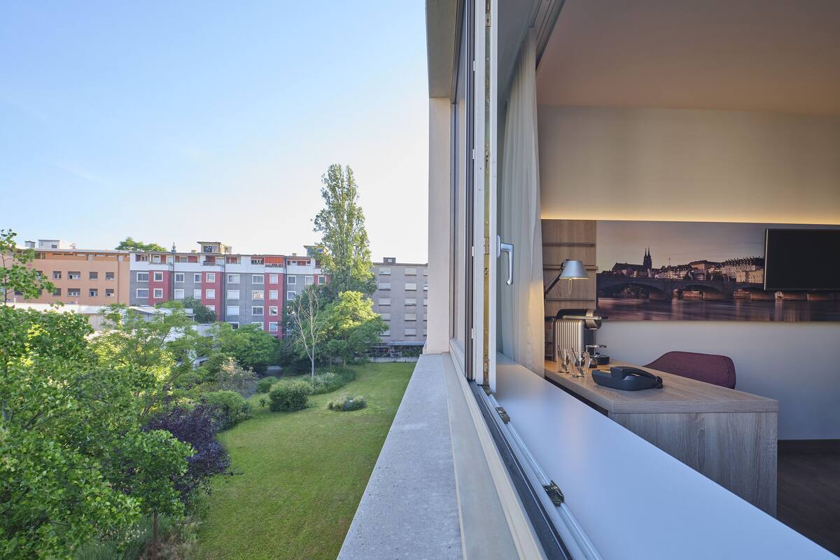 A modern hotel room with a balcony, a cityscape view, and a small dining area with a table and chairs.