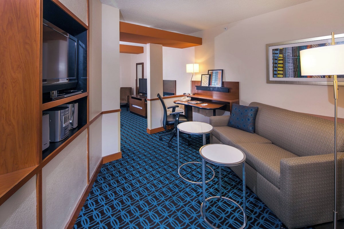 A compact hotel room with a sofa, a small desk with a chair, a television, and a lamp.