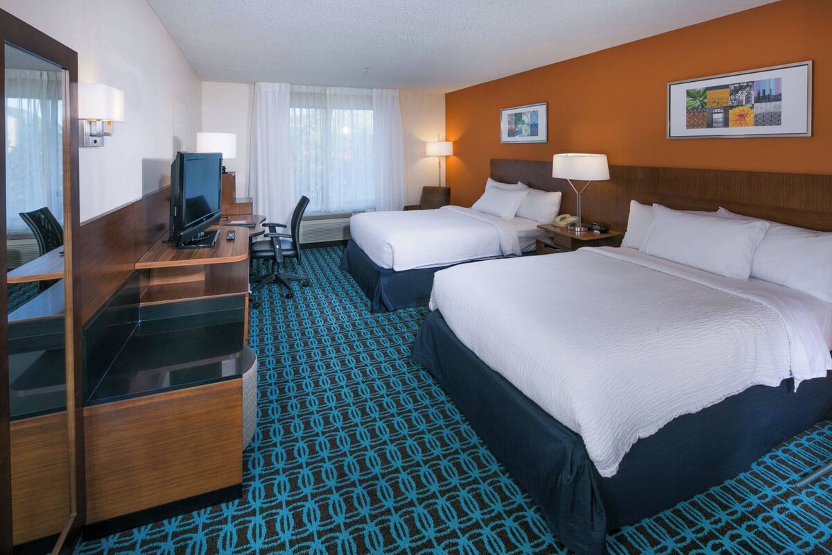 A hotel room with two beds, a desk with a computer, a chair, and a TV.