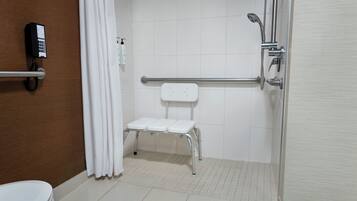 Un baño con un inodoro blanco, ducha con barra de apoyo y un banco blanco.