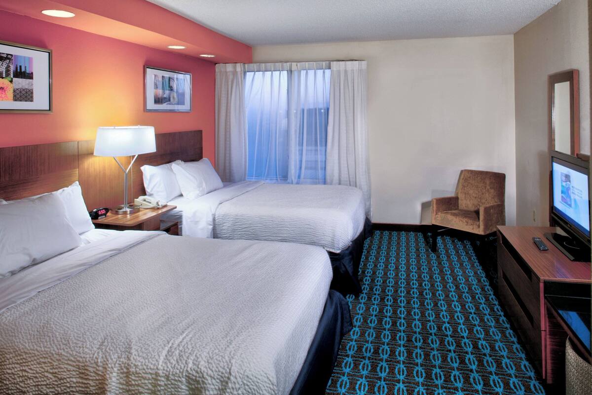 A hotel room with two beds, a TV, a desk, and a chair.