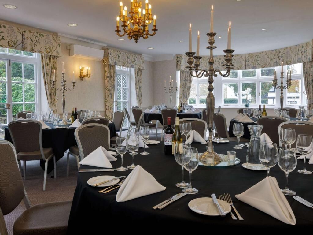 Comedor con mesas dispuestas para una comida, con candelabros y papel tapiz con motivos florales.