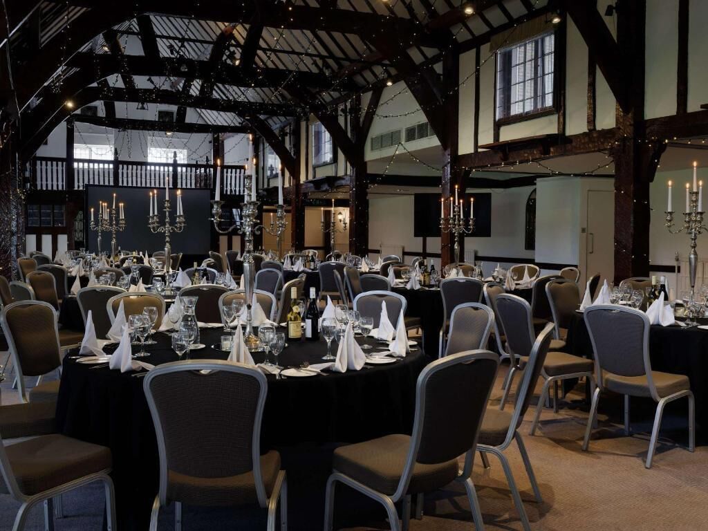 Un salón de banquetes con mesas redondas dispuestas para cenar, con candelabros y un techo alto con vigas a la vista.