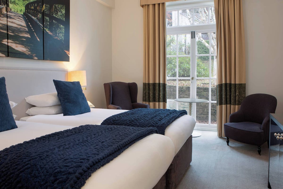 A hotel room with a large bed, two chairs, a small table, and a window with curtains.