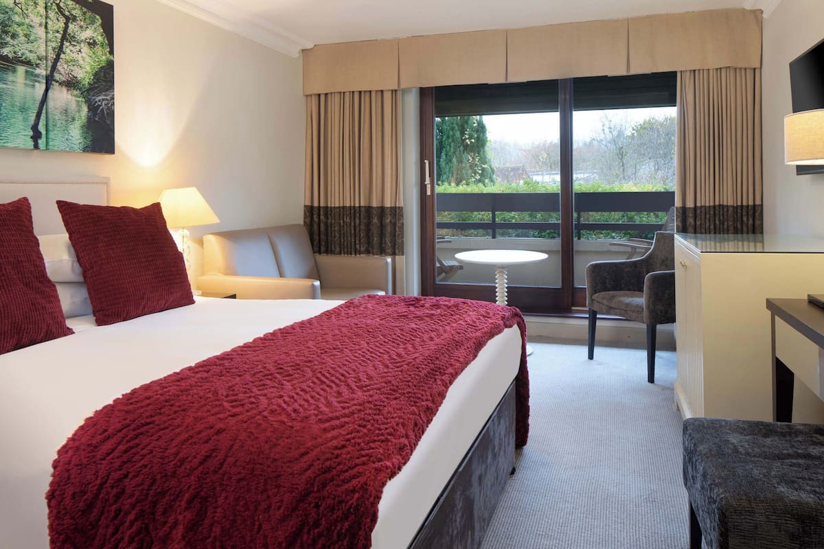 A hotel room with a large bed, a desk, a chair, and a balcony with a view.