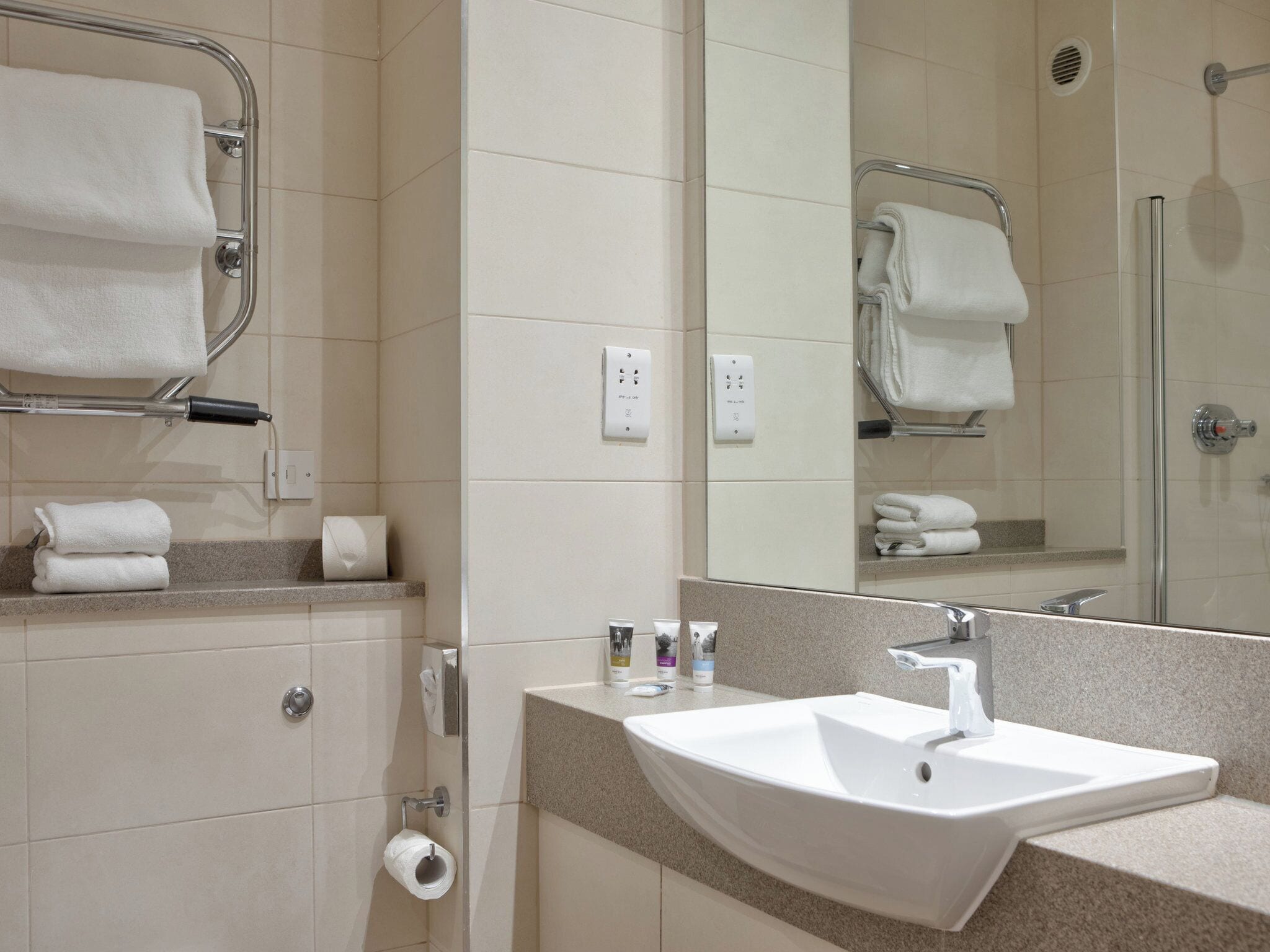 Un baño moderno con lavamanos, espejo, toallero y dispensador de papel higiénico.