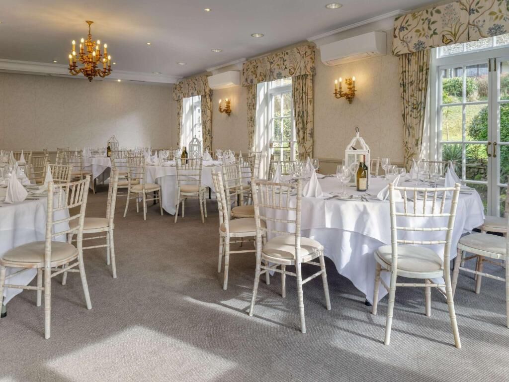 A banquet hall with multiple round tables, white tablecloths, and light-colored chairs.