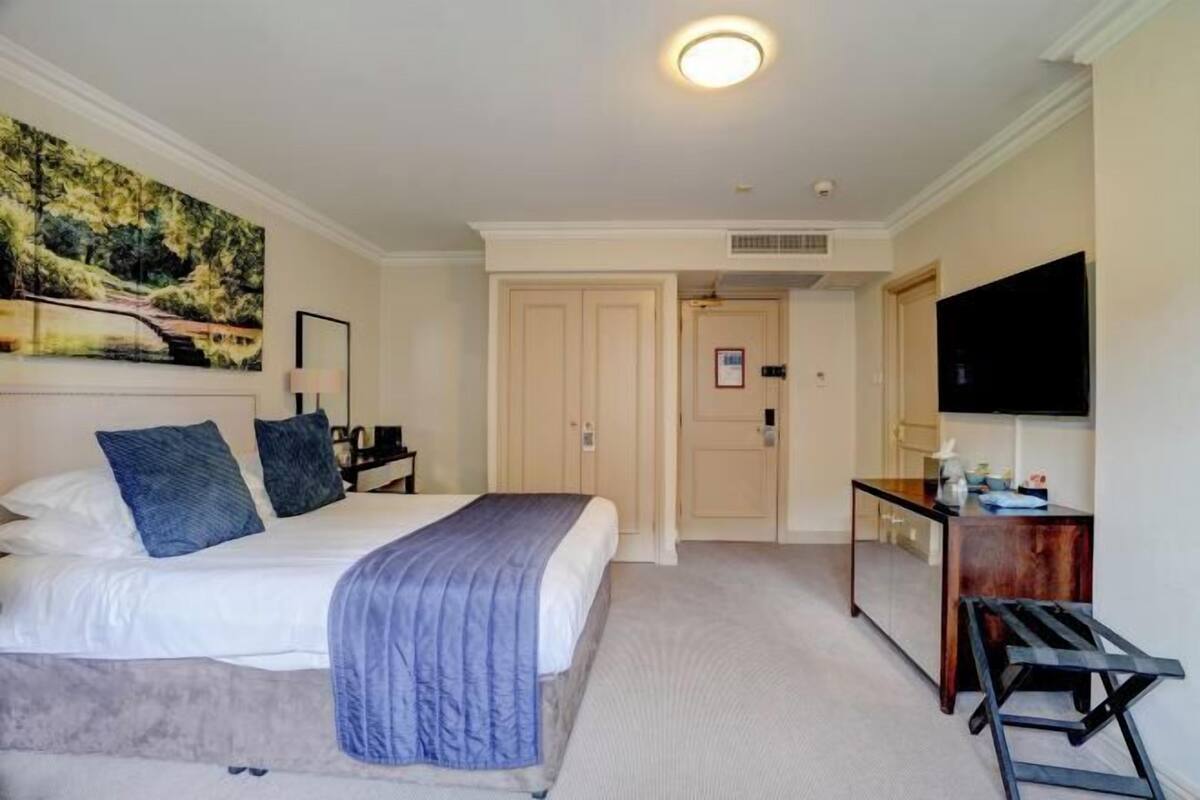 A hotel room with a bed, a desk, a television, and a door leading to another room.
