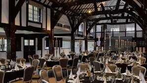 Un amplio salón de banquetes con varias mesas redondas dispuestas para comer, con manteles negros y servilletas blancas.
