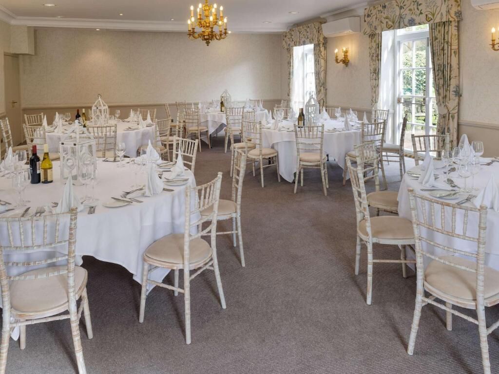 A banquet hall with round tables, white chairs, and chandeliers.