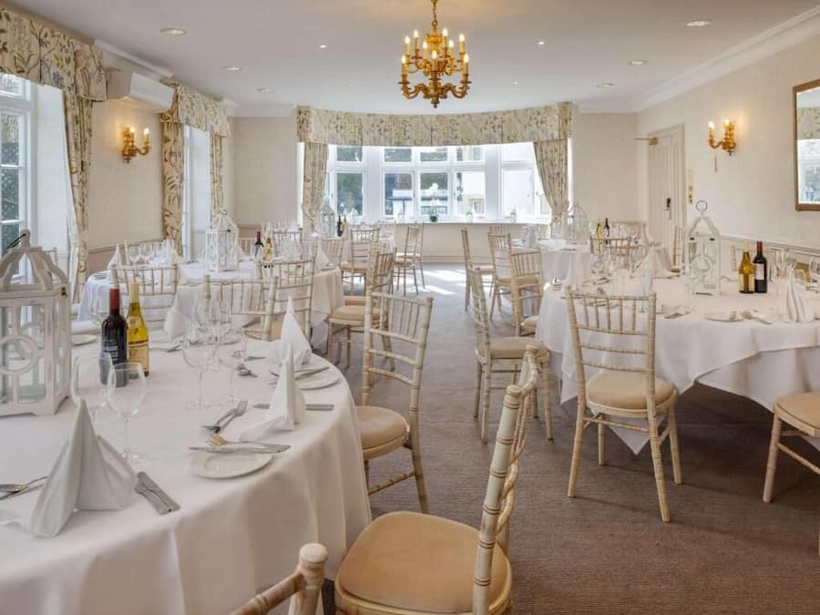 Un salón de banquetes con mesas redondas, manteles blancos y sillas de madera.