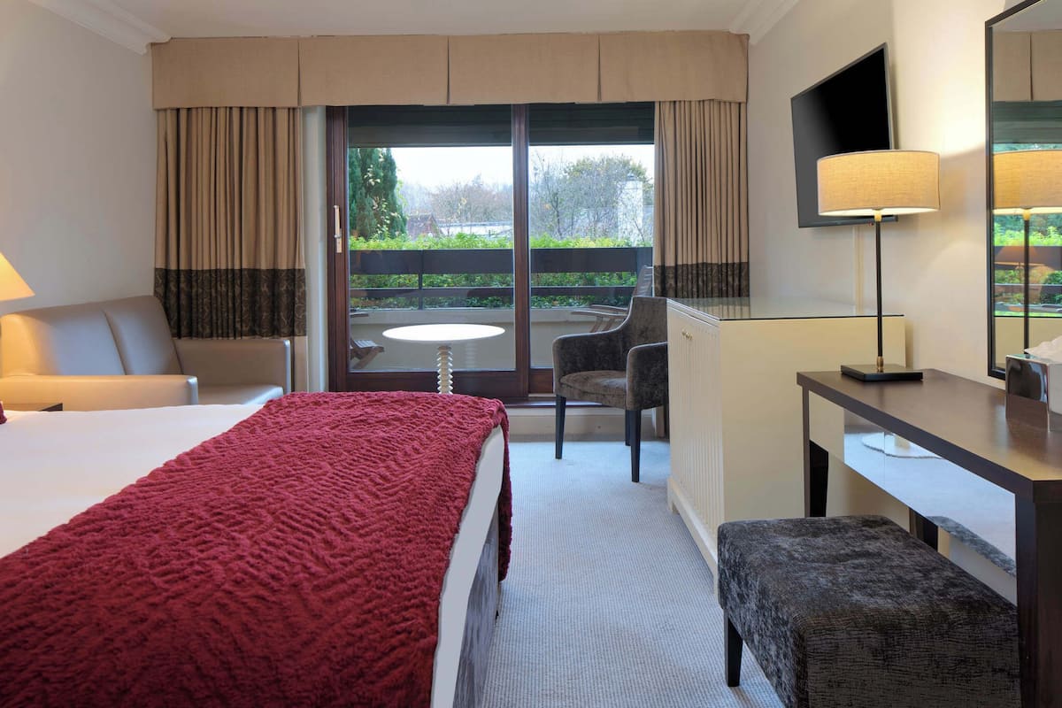 A hotel room with a bed, a desk, a chair, a sofa, and a balcony with a view.