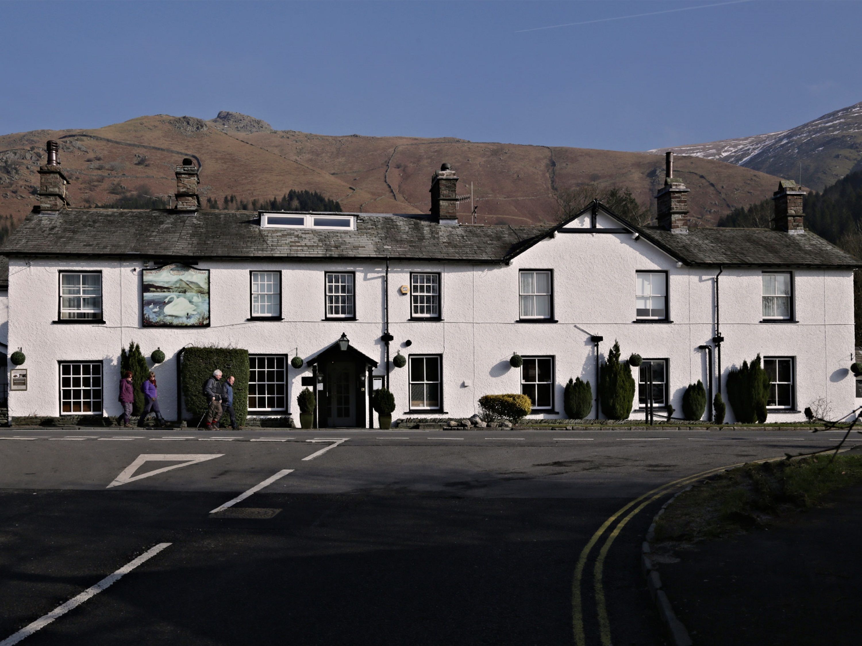 A white building with multiple windows and a signboard, located in a rural setting with mountains in the background.