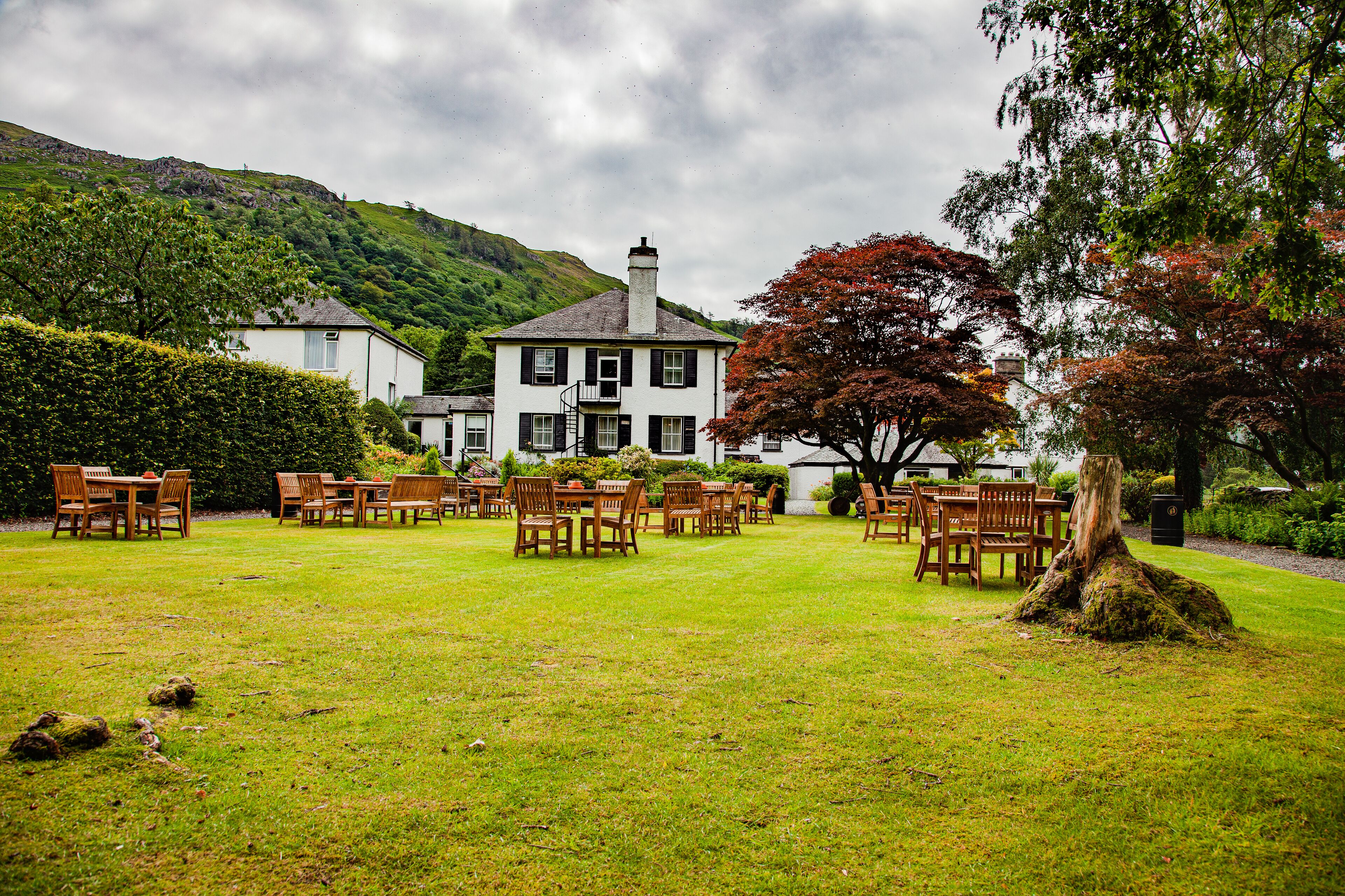 A white building with a chimney, surrounded by a grassy lawn with wooden tables and chairs.
