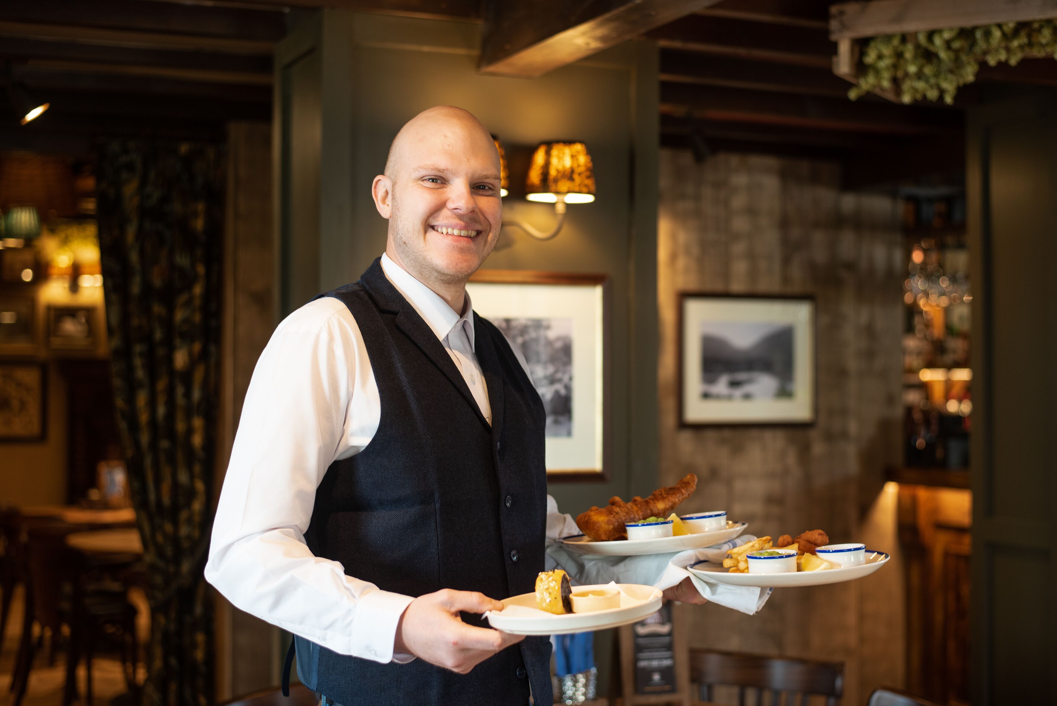 A waiter holding plates with food in a restaurant setting.