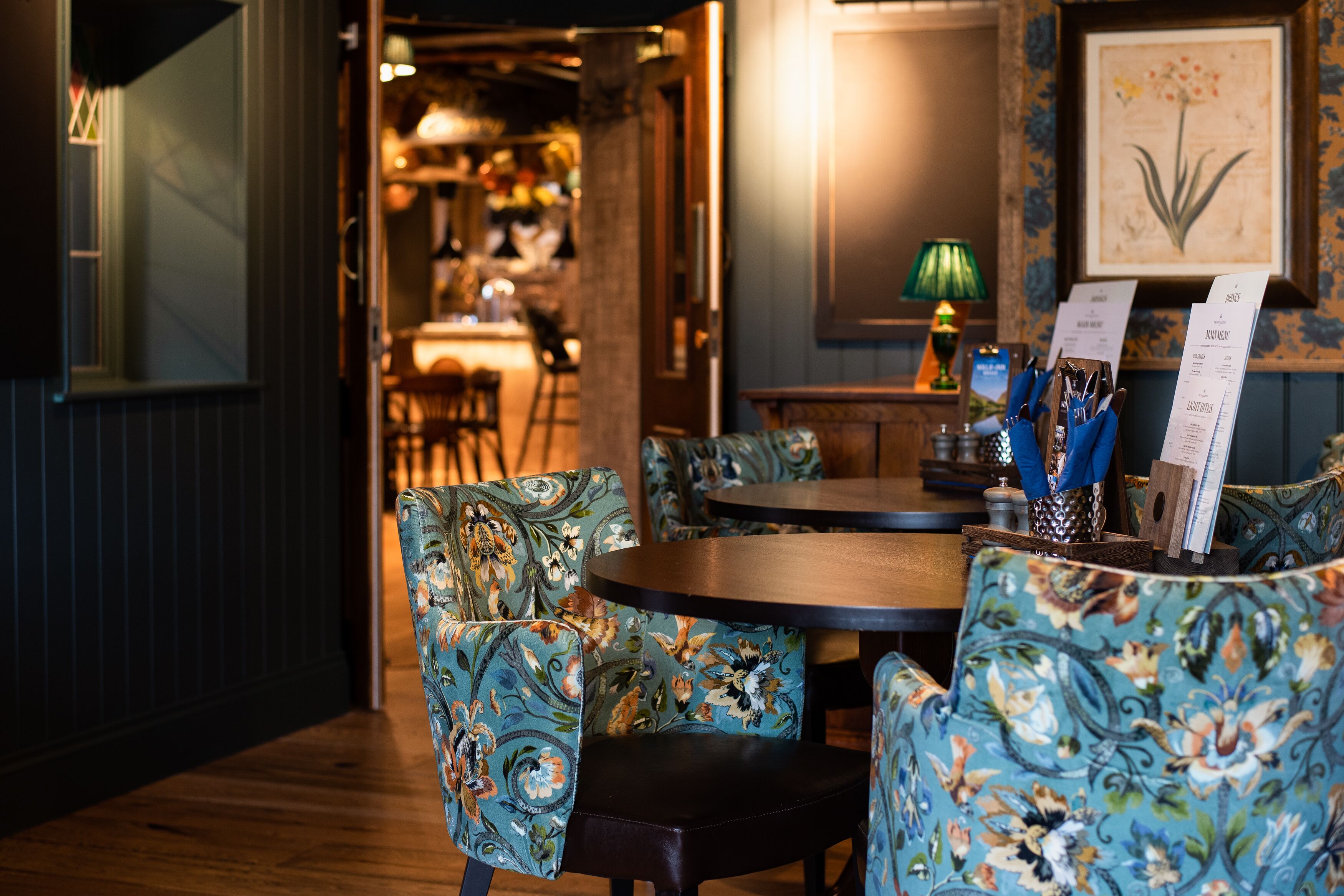 Un interior de restaurante con sillas de estampado floral, una mesa de madera y un atril para el menú.
